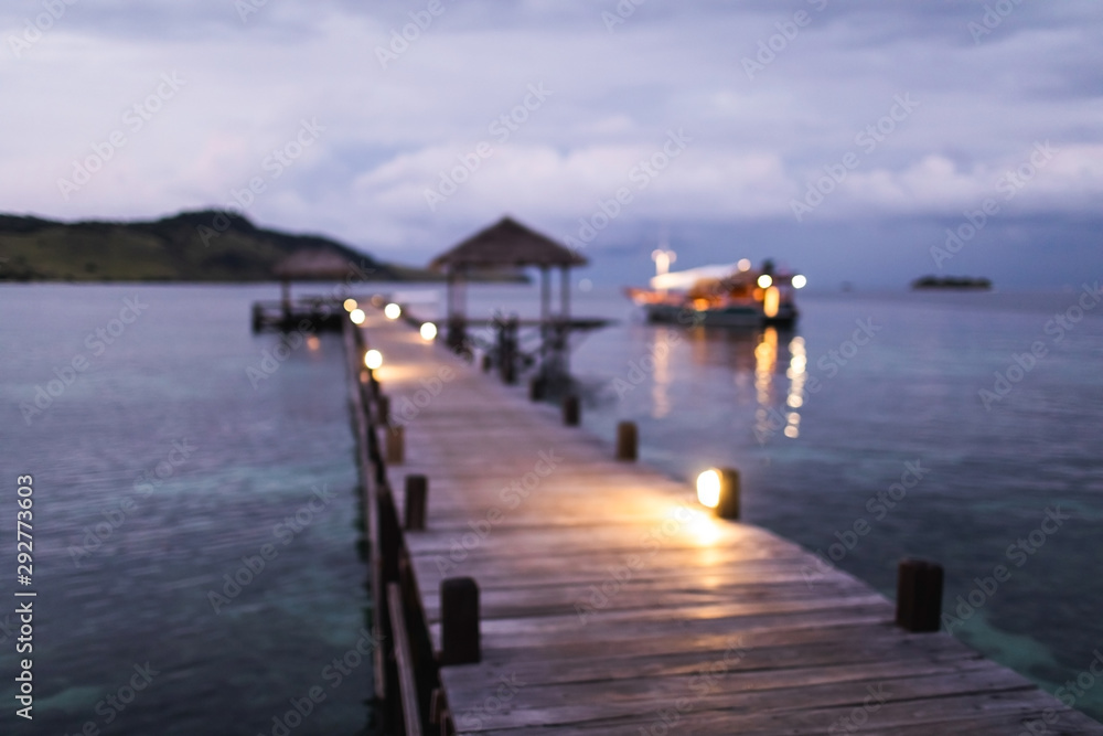 Blurred defocused background of tropical island, pier and yacht in twilight with evening lights in bokeh. Marine travel and vacations concept.
