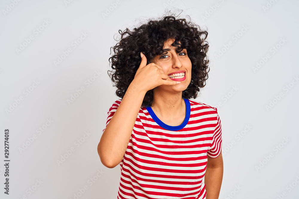 Young arab woman with curly hair wearing striped t-shirt over isolated white background smiling doing phone gesture with hand and fingers like talking on the telephone. Communicating concepts. Young arab woman with curly hair wearing striped t-shirt over isolated white background smiling doing phone gesture with hand and fingers like talking on the telephone. Communicating concepts.