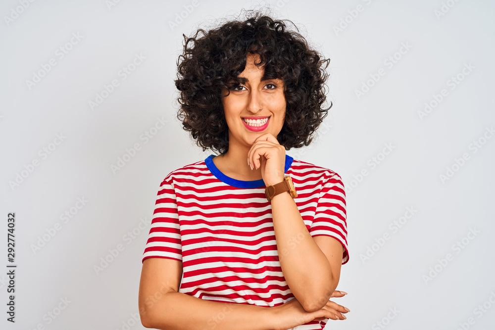 Young arab woman with curly hair wearing striped t-shirt over isolated white background looking confident at the camera smiling with crossed arms and hand raised on chin. Thinking positive. Young arab woman with curly hair wearing striped t-shirt over isolated white background looking confident at the camera smiling with crossed arms and hand raised on chin. Thinking positive.