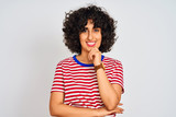 Young arab woman with curly hair wearing striped t-shirt over isolated white background looking confident at the camera smiling with crossed arms and hand raised on chin. Thinking positive.
