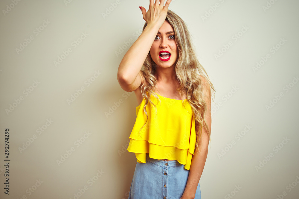 Young beautiful woman wearing yellow t-shirt standing over white isolated background surprised with hand on head for mistake, remember error. Forgot, bad memory concept. Young beautiful woman wearing yellow t-shirt standing over white isolated background surprised with hand on head for mistake, remember error. Forgot, bad memory concept.