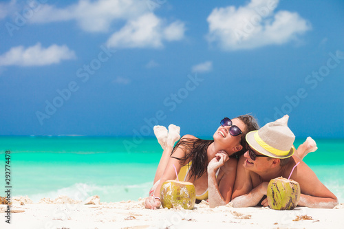 happy young couple lying on a tropical beach in Barbados and drinking a coconut cocktail