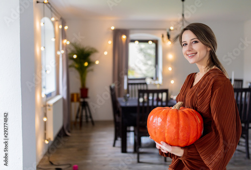 girl with a pumpkin is standing near the table at home, on the eve of the autumn holiday