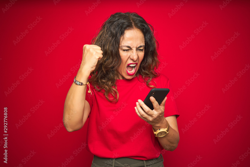 Naklejka premium Middle age senior woman using smartphone over red isolated background annoyed and frustrated shouting with anger, crazy and yelling with raised hand, anger concept