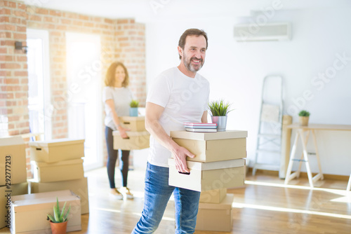 Middle age senior couple moving to a new house, man smiling happy in love with new apartment and holding cardboard boxes