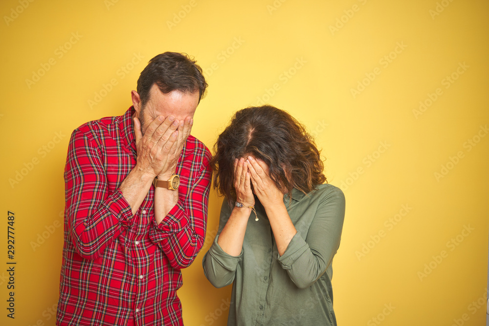 Beautiful middle age couple over isolated yellow background with sad expression covering face with hands while crying. Depression concept. Beautiful middle age couple over isolated yellow background with sad expression covering face with hands while crying. Depression concept.