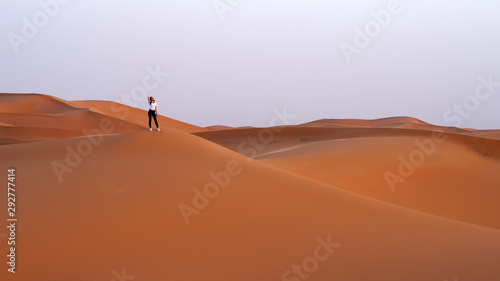 Female traveler stands on top of a sand dune in the Sahara desert, vacation in Morocco.