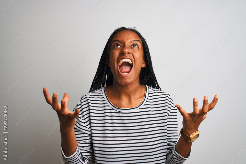 Young african american woman wearing striped t-shirt standing over isolated white background crazy and mad shouting and yelling with aggressive expression and arms raised. Frustration concept. Young african american woman wearing striped t-shirt standing over isolated white background crazy and mad shouting and yelling with aggressive expression and arms raised. Frustration concept.