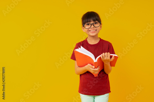 Young Asia girl student with big smiled wearing glasses and red shirt open and read  book on yellow background in studio