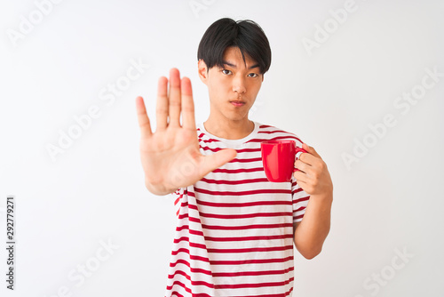 Young chinese man drinking a cup of coffee standing over isolated white background with open hand doing stop sign with serious and confident expression, defense gesture