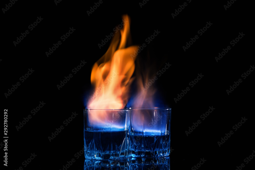 Close up, macro. Two glasses with cocktails, on the surface of which a blue-orange flame quivers. Black background. Copy space. Close up, macro. Two glasses with cocktails, on the surface of which a blue-orange flame quivers. Black background. Copy space.