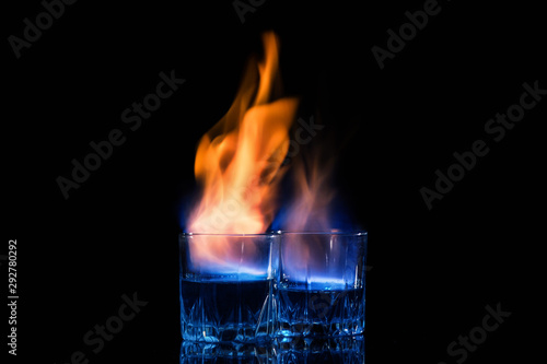 Close up, macro. Two glasses with cocktails, on the surface of which a blue-orange flame quivers. Black background. Copy space.