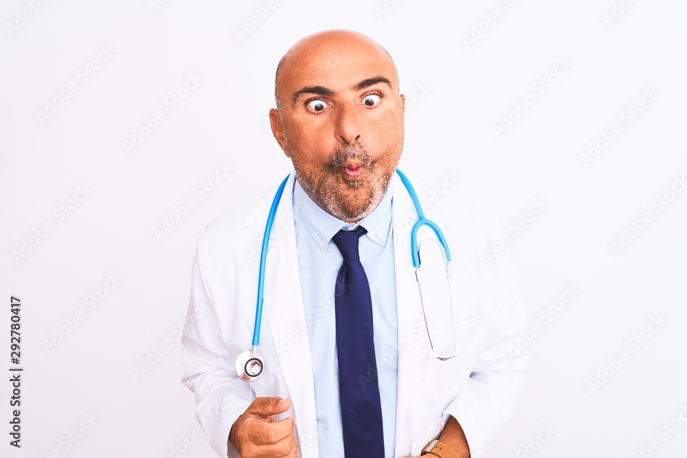 Middle age doctor man wearing stethoscope and tie standing over isolated white background making fish face with lips, crazy and comical gesture. Funny expression. Middle age doctor man wearing stethoscope and tie standing over isolated white background making fish face with lips, crazy and comical gesture. Funny expression.
