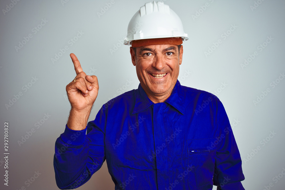 Handsome middle age worker man wearing uniform and helmet over isolated white background pointing finger up with successful idea. Exited and happy. Number one.