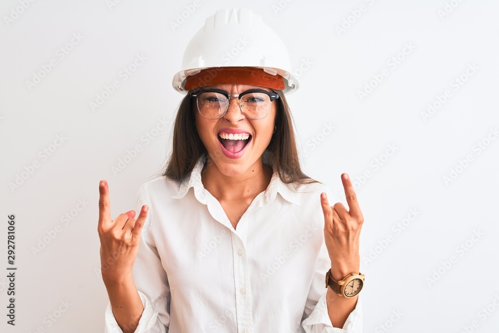 Young beautiful architect woman wearing helmet and glasses over isolated white background shouting with crazy expression doing rock symbol with hands up. Music star. Heavy concept.