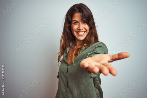 Canvas-taulu Young beautiful woman wearing green shirt standing over grey isolated background smiling cheerful offering palm hand giving assistance and acceptance