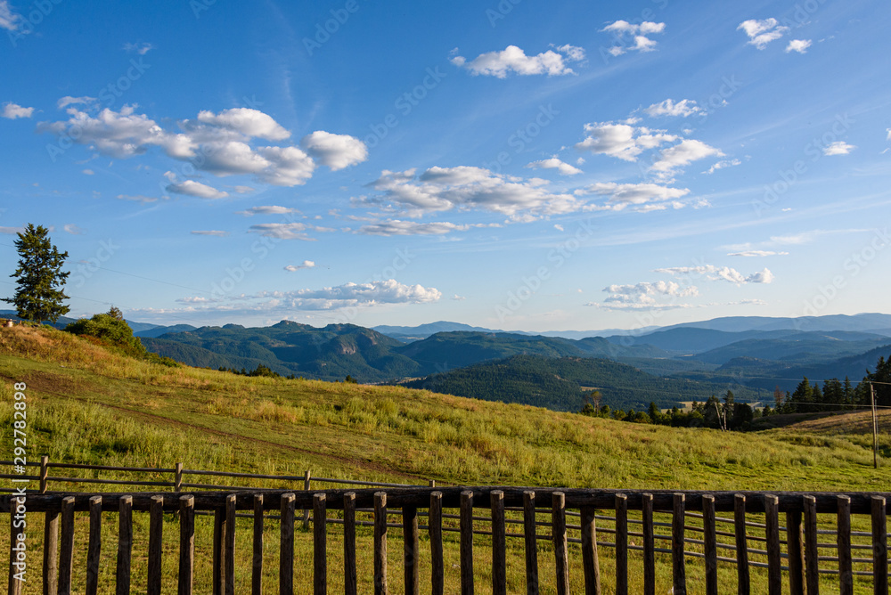 View from hilltop deck, behind railing, landscape of rolling hills, forests, and cloudy sky, Eastern Washington state, USA