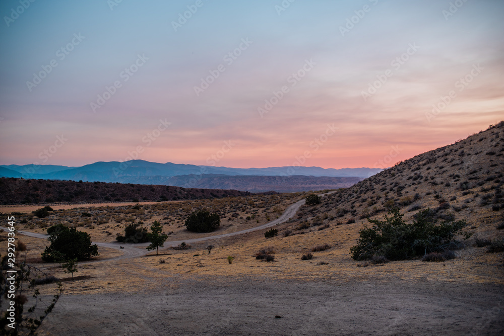 Fototapeta premium Pink desert sunset over remote desert road and blue mountains