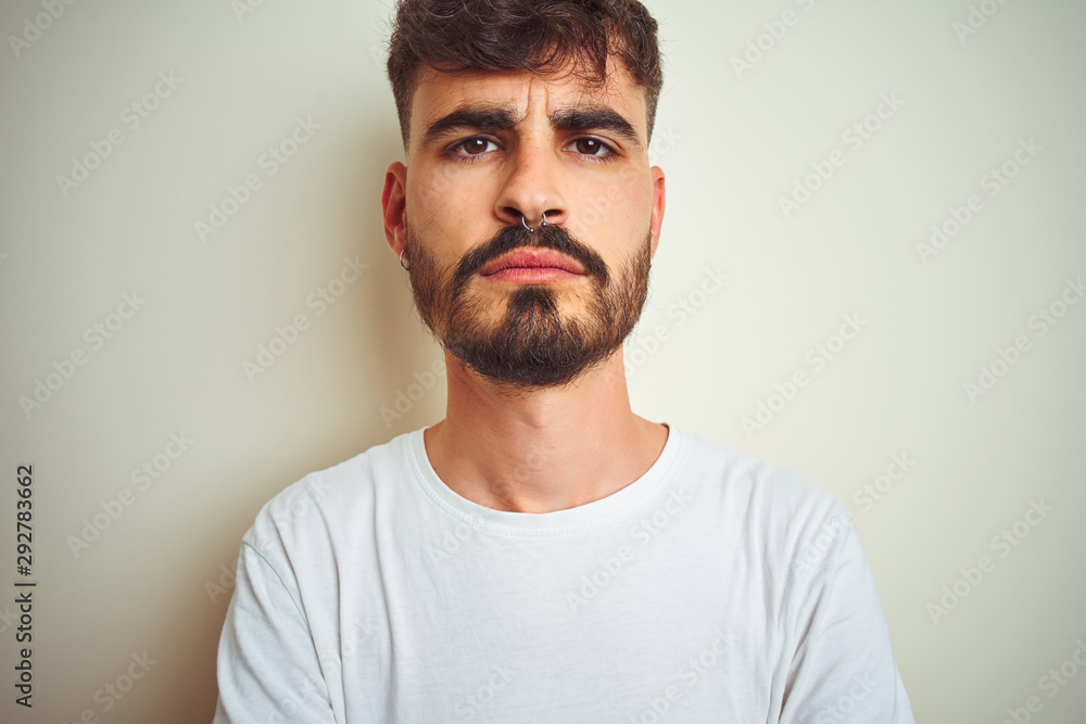 Young man with tattoo wearing t-shirt standing over isolated white background skeptic and nervous, disapproving expression on face with crossed arms. Negative person. Young man with tattoo wearing t-shirt standing over isolated white background skeptic and nervous, disapproving expression on face with crossed arms. Negative person.