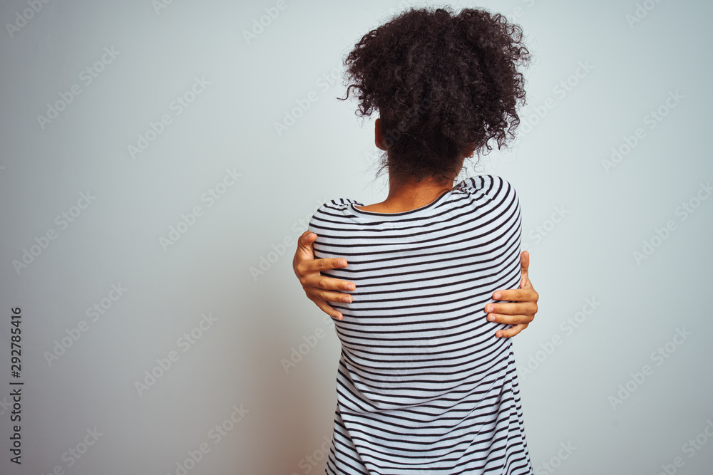African american woman wearing navy striped t-shirt standing over isolated white background Hugging oneself happy and positive from backwards. Self love and self care African american woman wearing navy striped t-shirt standing over isolated white background Hugging oneself happy and positive from backwards. Self love and self care