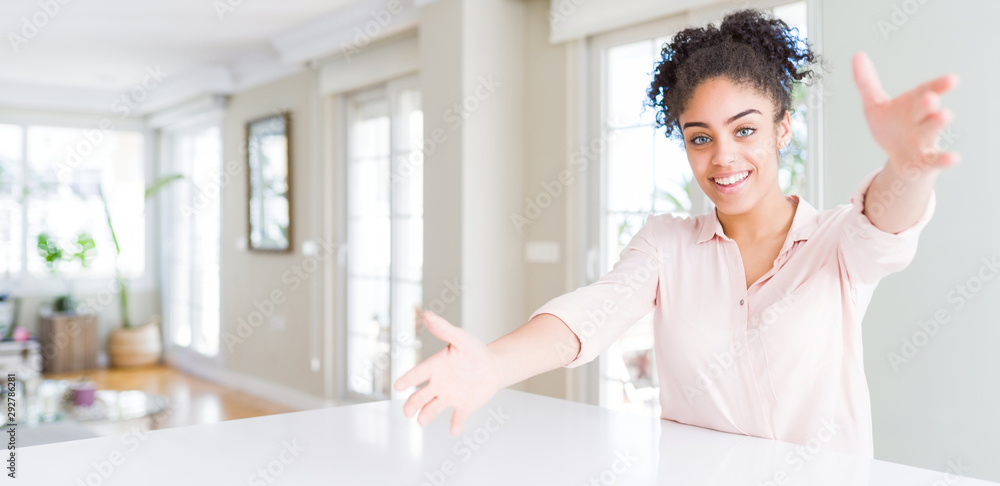 Wide angle of beautiful african american woman with afro hair looking at the camera smiling with open arms for hug. Cheerful expression embracing happiness. Wide angle of beautiful african american woman with afro hair looking at the camera smiling with open arms for hug. Cheerful expression embracing happiness.