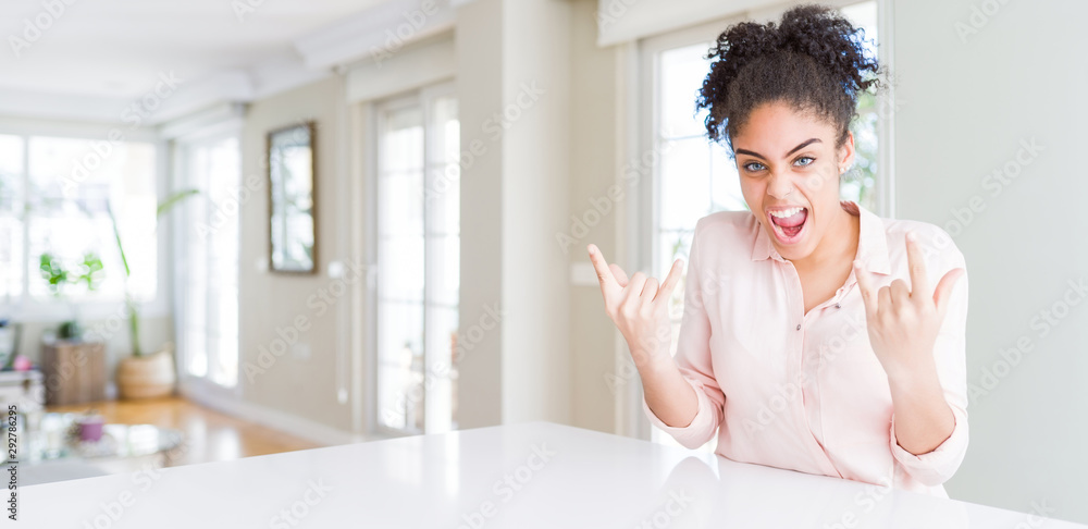 Wide angle of beautiful african american woman with afro hair shouting with crazy expression doing rock symbol with hands up. Music star. Heavy music concept.