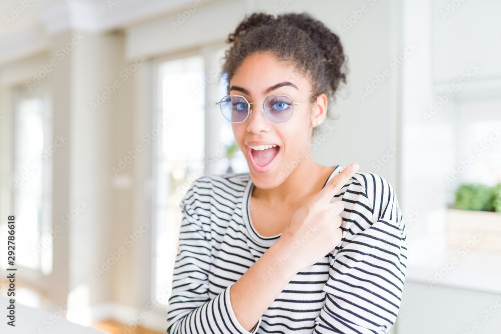 Beautiful young african american woman with afro hair wearing glasses cheerful with a smile of face pointing with hand and finger up to the side with happy and natural expression on face