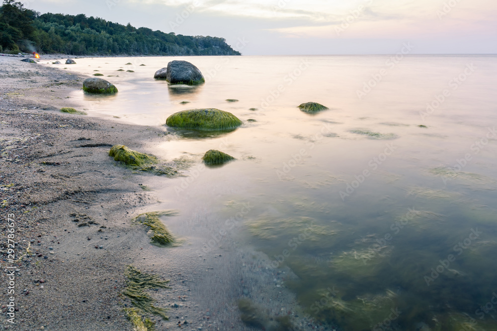 landscape of the sea coast with large boulders in the water, covered with mud in twilight light at long exposure