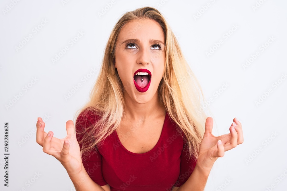 Young beautiful woman wearing red t-shirt standing over isolated white background crazy and mad shouting and yelling with aggressive expression and arms raised. Frustration concept. Young beautiful woman wearing red t-shirt standing over isolated white background crazy and mad shouting and yelling with aggressive expression and arms raised. Frustration concept.