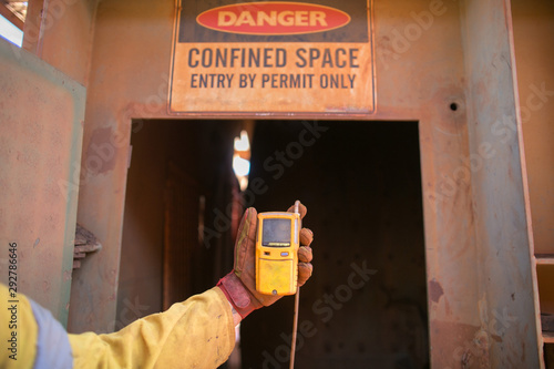 Constructor worker hand holding gas test leak detector device while commencing safety gas testing atmosphere at main entry and exit on confined space door prior to work construction site, Australia 