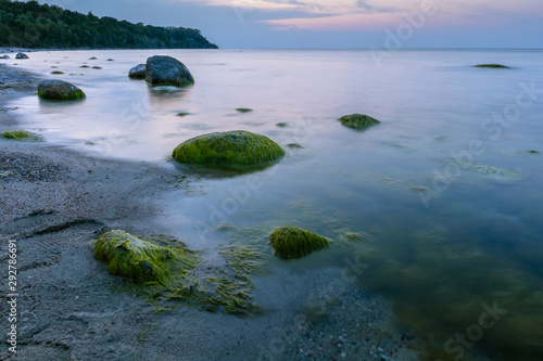 landscape of the sea coast with large boulders in the water, covered with mud in blue twilight light at long exposure