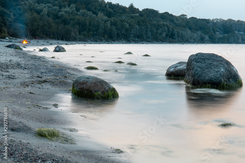 landscape of the sea coast with the forest in the background, large boulders in the water, covered with mud in twilight light at a long exposure