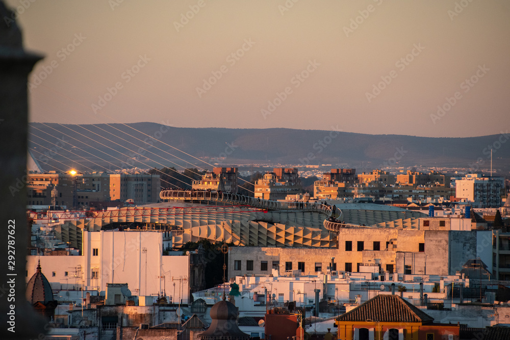 A view of the Spanish city of Sevilla during an orange sunset with the Metropol Parasol peaking through the buildings