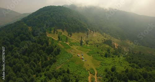 An aerial shot of a group of people camping over a mountain 3 An unveiling shot of some offroad 4wheel cars and visitors camp area in a great green nature under beautiful clouds   photo