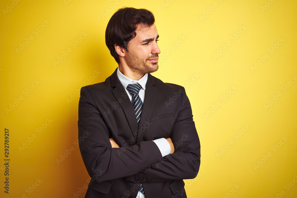 Young handsome businessman wearing suit and tie standing over isolated yellow background looking to the side with arms crossed convinced and confident Young handsome businessman wearing suit and tie standing over isolated yellow background looking to the side with arms crossed convinced and confident