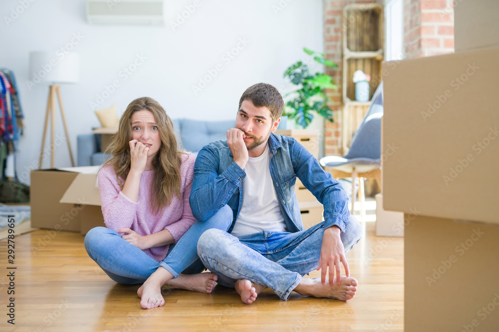 Young beautiful couple moving to a new house sitting on the floor looking stressed and nervous with hands on mouth biting nails. Anxiety problem. Young beautiful couple moving to a new house sitting on the floor looking stressed and nervous with hands on mouth biting nails. Anxiety problem.