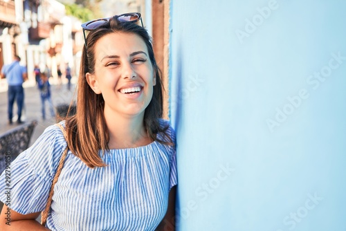 Beautiful girl leaning on blue wall, young friendly woman smiling happy on a sunny day of summer