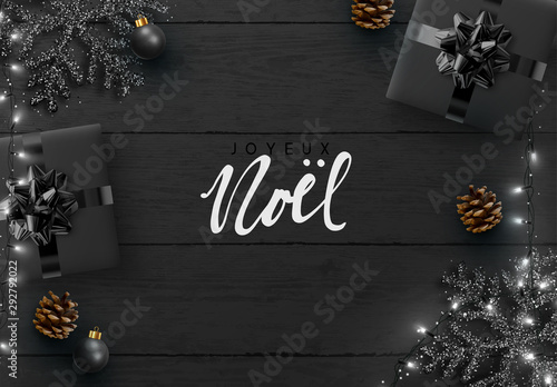French text Joyeux Noel. Christmas background. Wood plank texture, black snowflakes, realistic pine cone, decorative baubles, gift boxes, xmas bright light white garland. Flat lay, top view