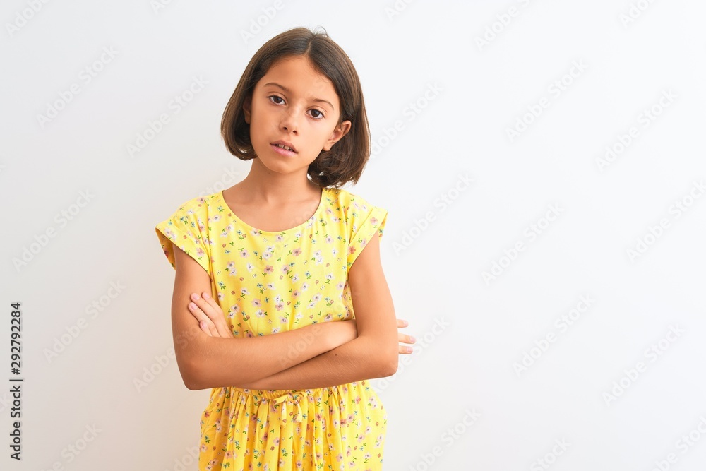 Young beautiful child girl wearing yellow floral dress standing over isolated white background skeptic and nervous, disapproving expression on face with crossed arms. Negative person. Young beautiful child girl wearing yellow floral dress standing over isolated white background skeptic and nervous, disapproving expression on face with crossed arms. Negative person.