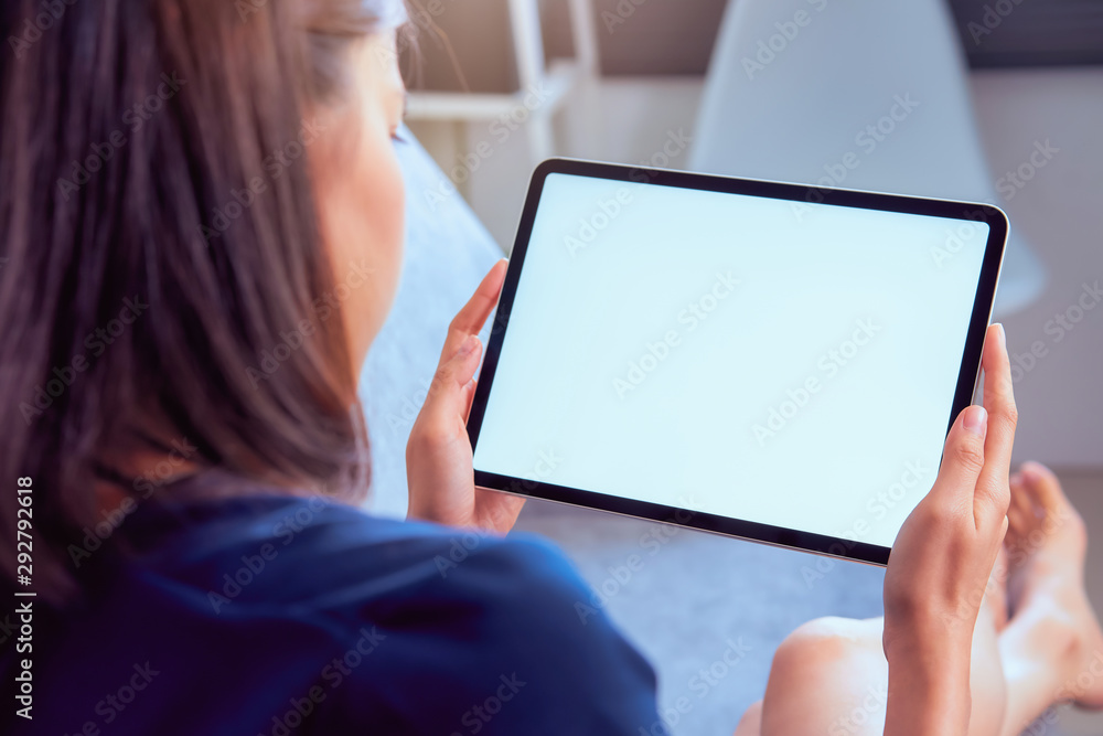 Young woman holding tablet with blank screen on the sofa in house.