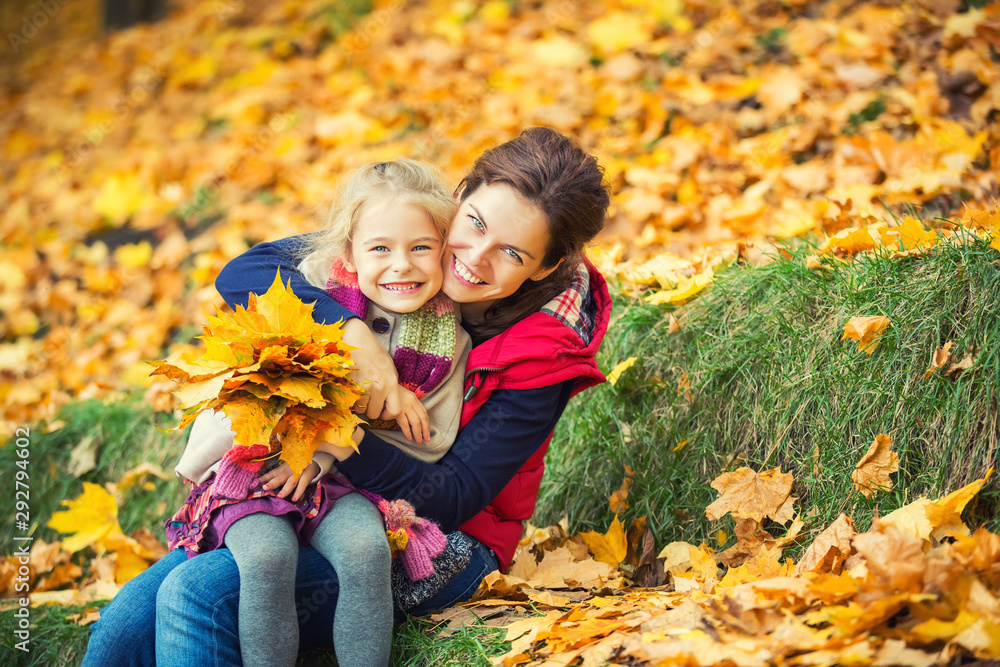 Happy little girl and her mother enjoy autumn park and play with bright autumn leaves Happy little girl and her mother enjoy autumn park and play with bright autumn leaves