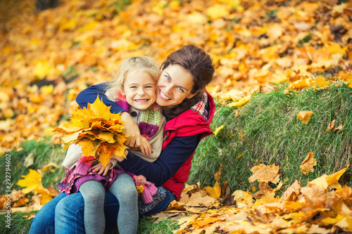 Happy little girl and her mother enjoy autumn park and play with bright autumn leaves