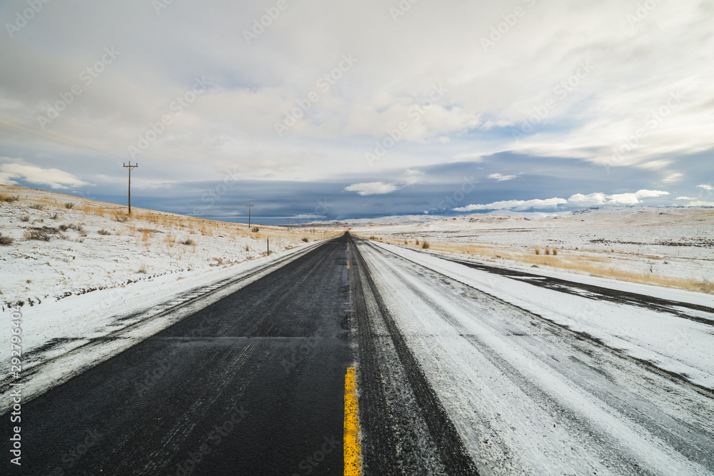Long straight road half covered with snow on a cloudy morning in Idaho, USA Long straight road half covered with snow on a cloudy morning in Idaho, USA