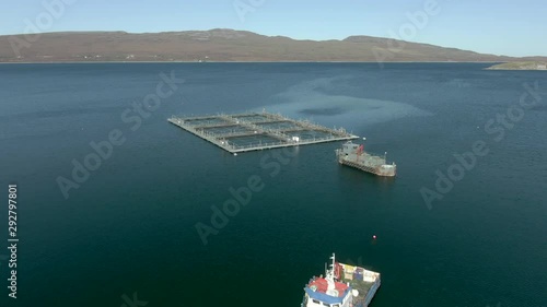 An aerial view of an aquaculture installation on Loch Eriboll in the Scottish Highlands on a sunny day. Ascending over the installation whilst tilting downwards towards it. photo