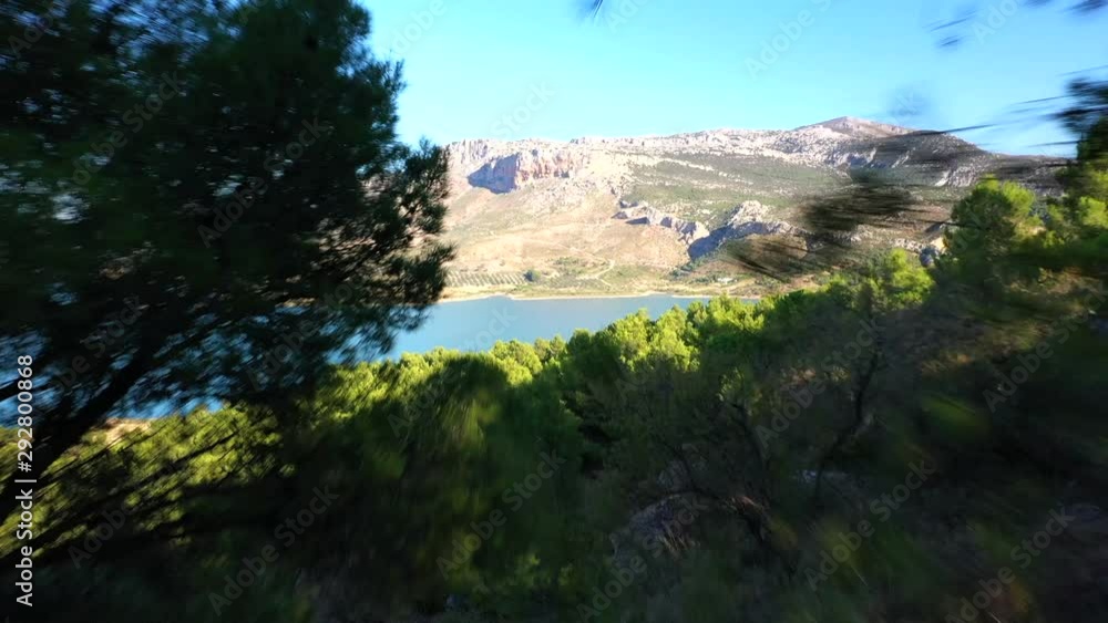Aerial view flying through small hole in between pine trees with a drone, flying through a tight gap to reveal a beautiful lake and mountain landscape Aerial view flying through small hole in between pine trees with a drone, flying through a tight gap to reveal a beautiful lake and mountain landscape