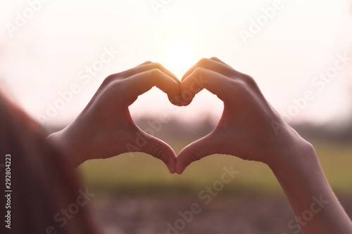 The person hand shows the heart shape symbol on the sunset background