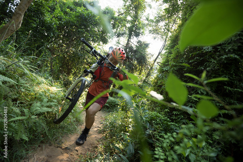 Woman cyclist carry a mountain bike walking on tropical forest trail