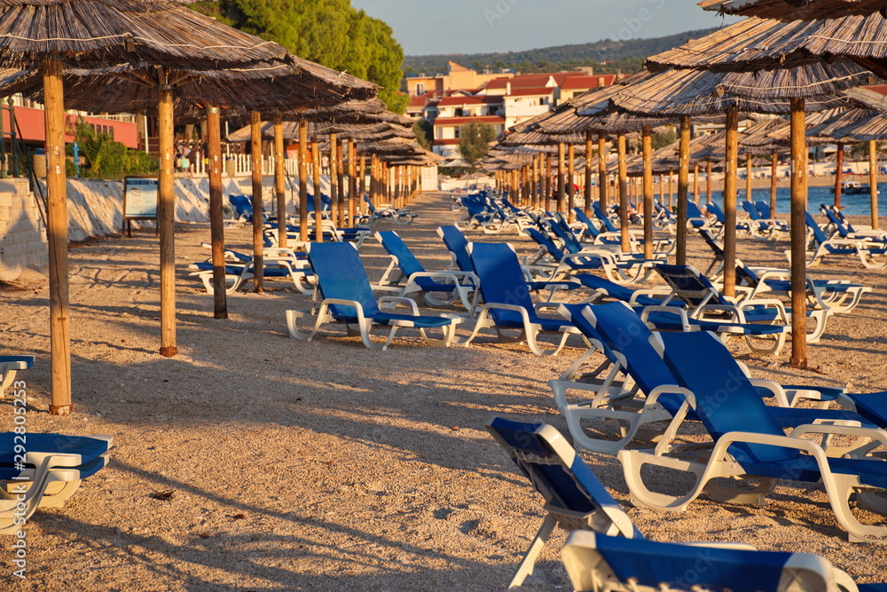 Group of parasols and beach chairs on the beach in Primosten in sunset Group of parasols and beach chairs on the beach in Primosten in sunset