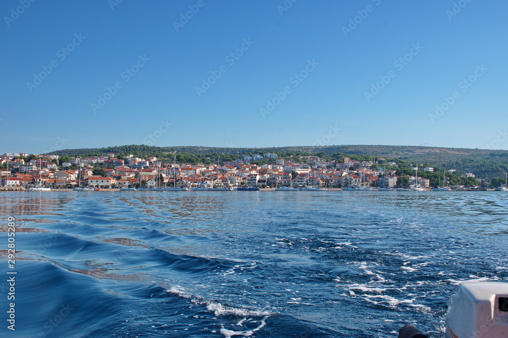 Sailing on motor boat on Adriatic sea with Primosten cityscape in the background. Vacation in Croatia