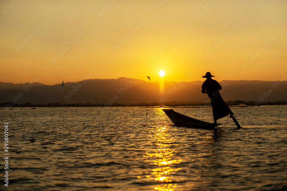 The silhouette of a fisherman on a boat at dusk The sunset is a beautiful orange sky. Inle Lake is a fresh water lake in the mountainous region of Shan State in Myanmar.